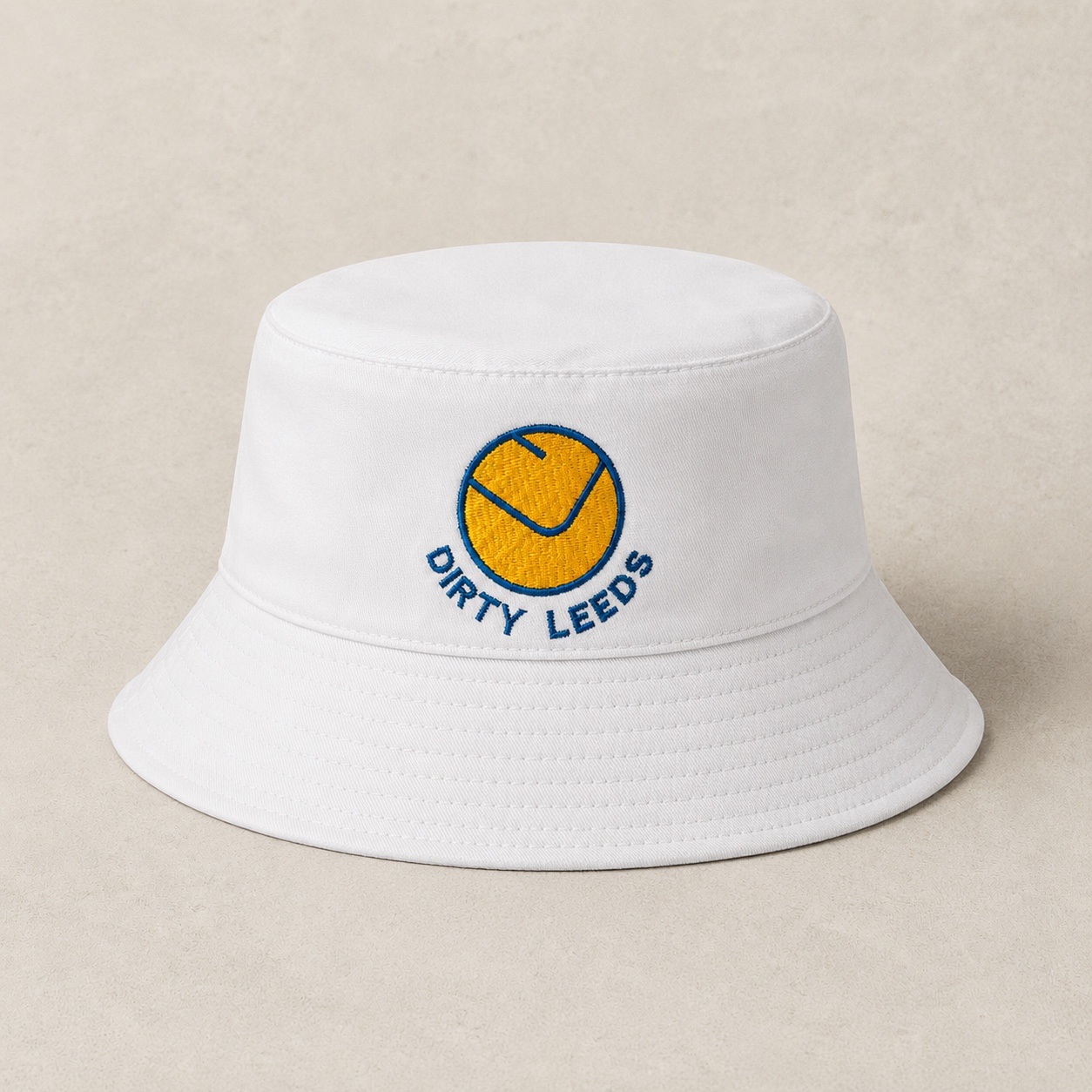 Front view of the white bucket hat with yellow and blue smiley badge and blue Dirty Leeds embroidery.