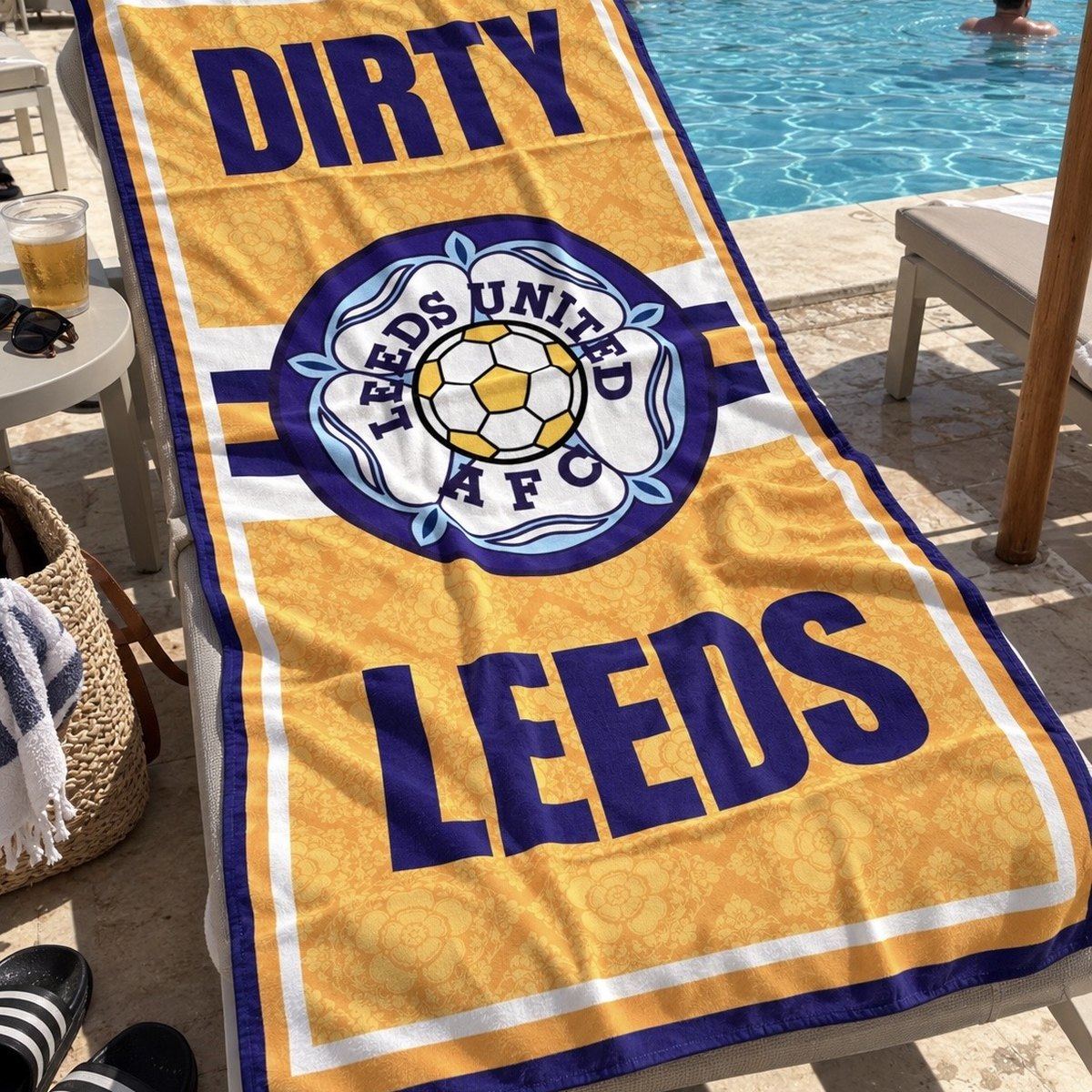 Dirty Leeds® XL Luxury Leeds United beach towel draped over a sunbed beside a hotel pool.