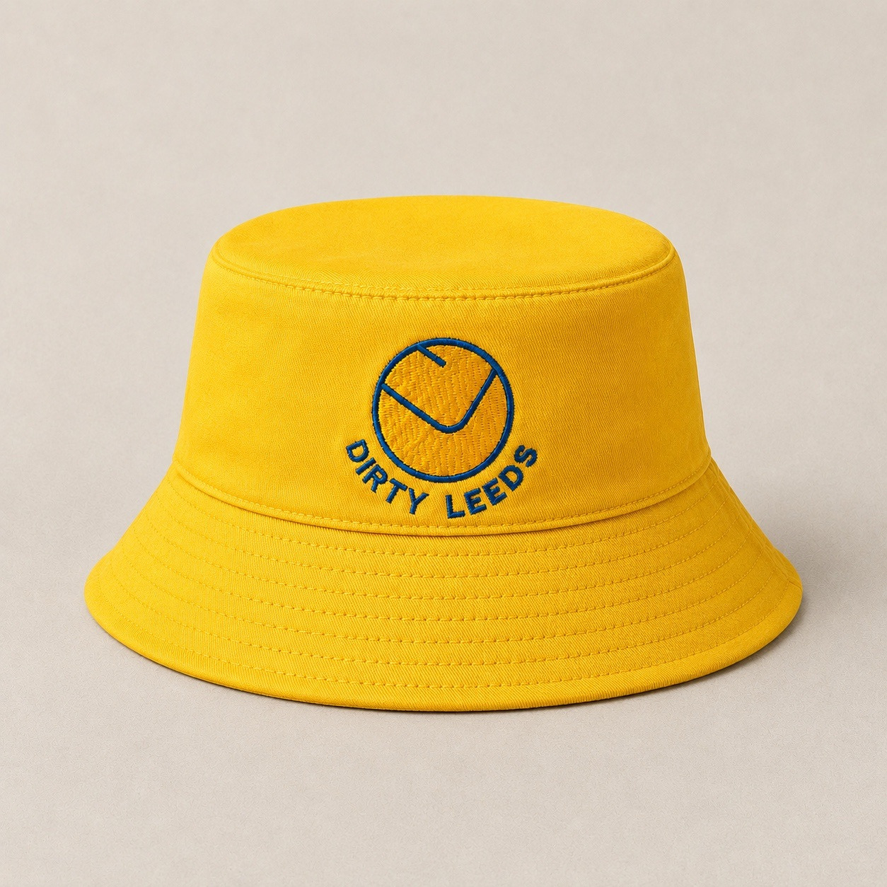 Front view of the yellow bucket hat with yellow and blue smiley badge and blue Dirty Leeds embroidery.