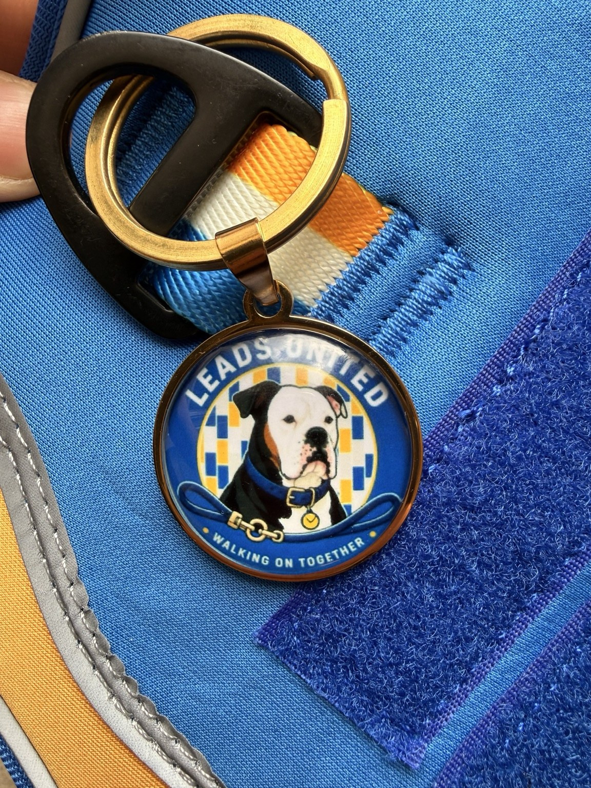 Close view of the round brass Leads United identity tag attached to the front metal ring.